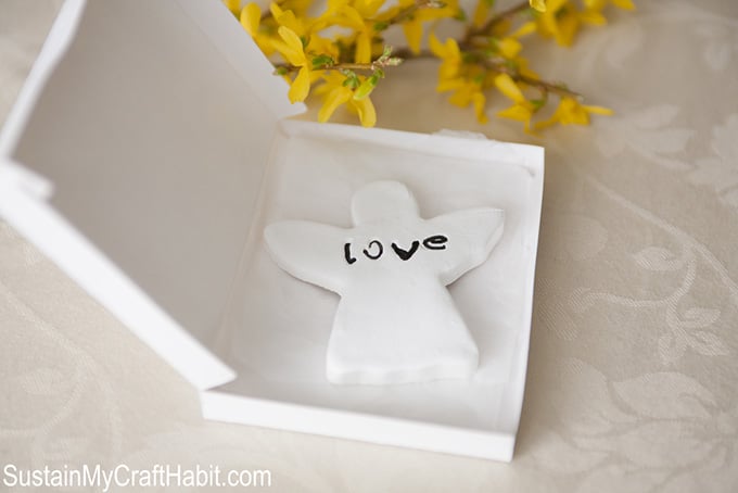 A small gift boxed filled with an angel-shaped ornament with the work love inscribed as a first communion favor idea