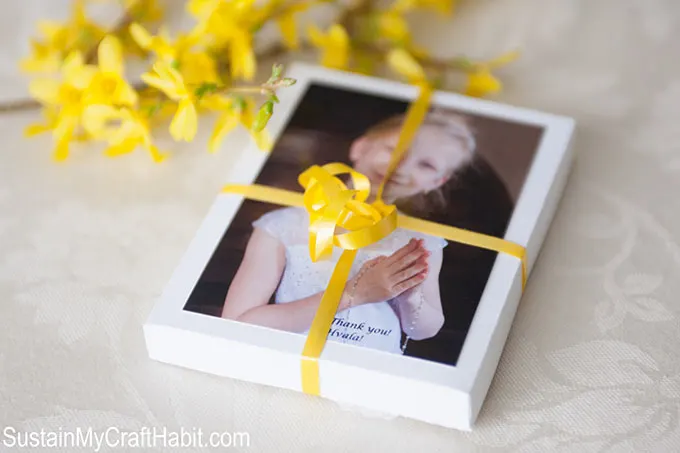Photo of a little girl in her first communion dress attached to a gift box with a yellow ribbon