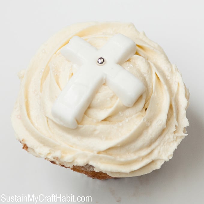 Vanilla frosted cupcake embellished with a white cross made with fondant and small silver edible bead