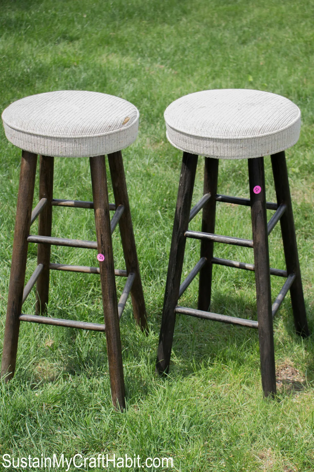 Two bar stools with dark brown legs and light fabric upholstery on the grass.