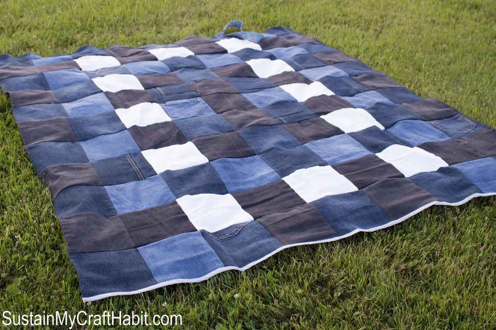 The DIY checkered denim picnic blanket laid out on the grass.
