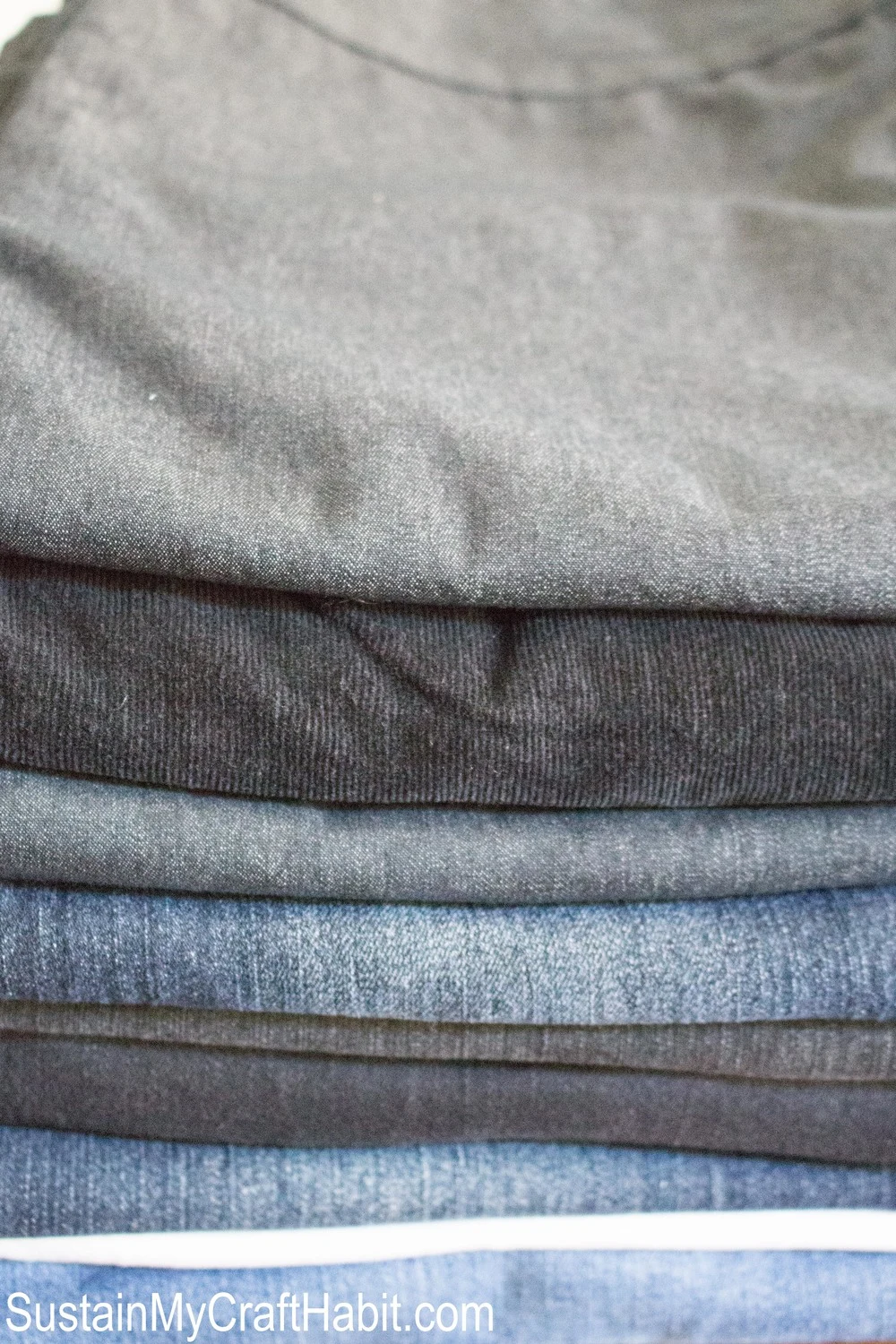 Close up view of a stack of old jeans showing different shades of blue and gray denim fabric.