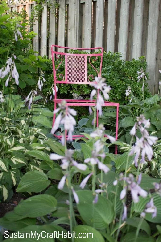 Bright pink painted cast iron patio chair in a lush green garden.