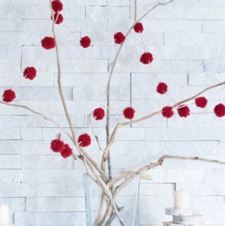 A DIY pom pom garland strung around driftwood branches as a part of a rustic Christmas mantel decorating idea