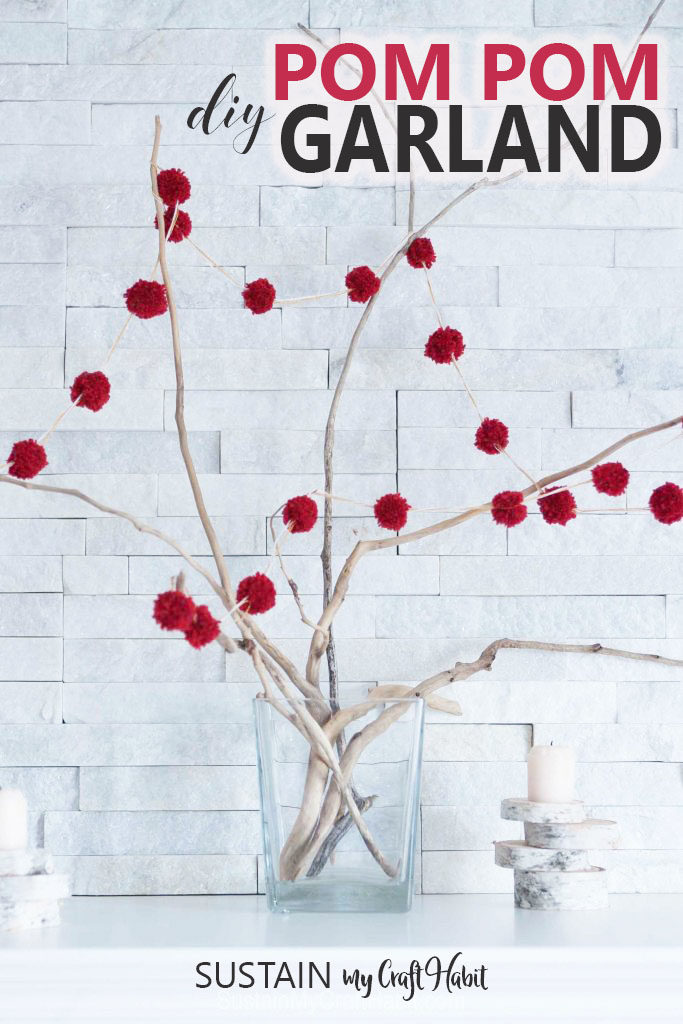 Red DIY pom pom garland strung on branches in a vase on a fireplace mantel