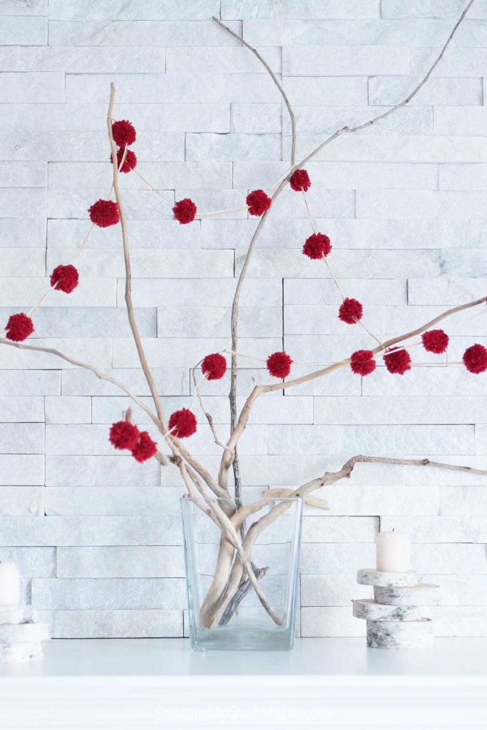 A DIY pom pom garland strung around driftwood branches as a part of a rustic Christmas mantel decorating idea