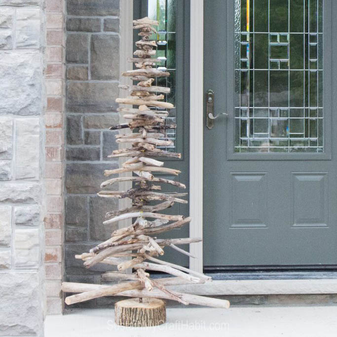 A rustic DIY driftwood Christmas tree on a front porch in front of a gray door