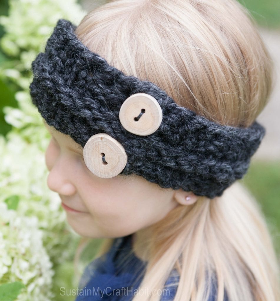 A blond child wearing a knitted headband pattern with handmade driftwood buttons