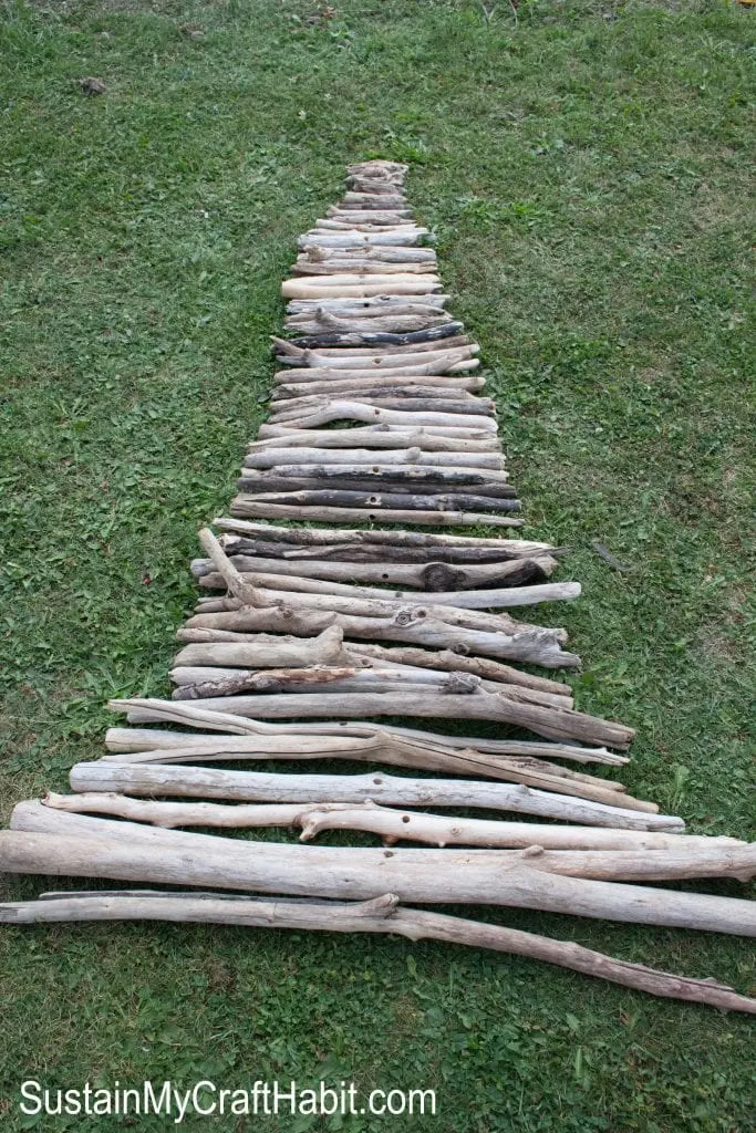 Lining up different length of driftwood branches on the grass to make a Christmas tree shape