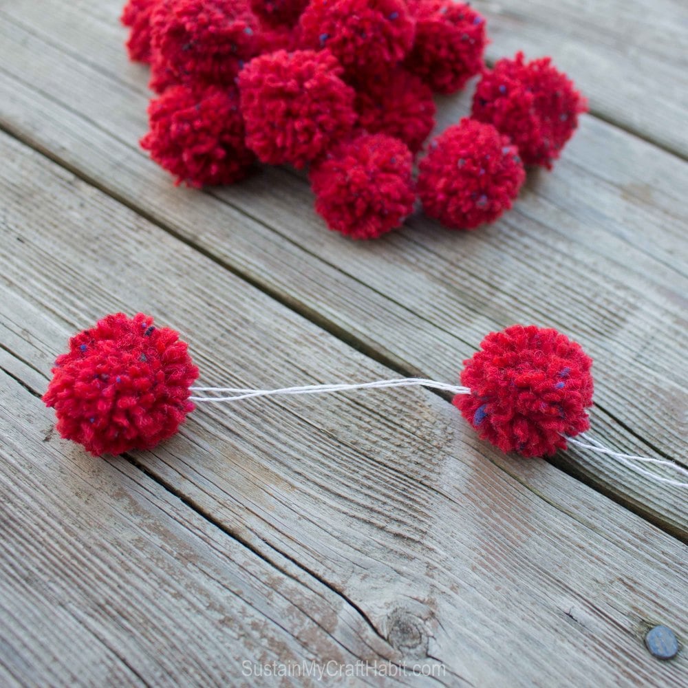 Two red pom poms joined together with white single ply yarn.