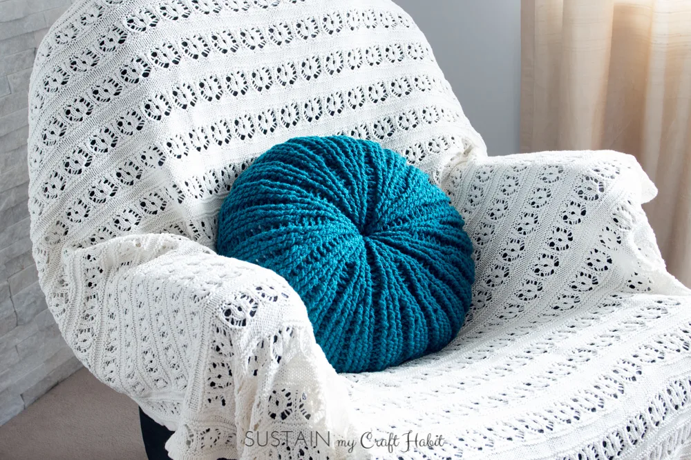Completed sand dollar crochet pillow cover on a chair covered with a white knitted blanket
