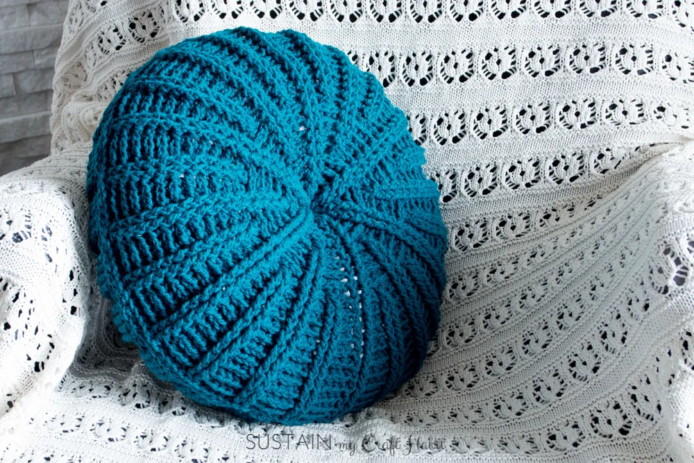 Teal wool round crochet throw pillow made from free crochet pillow patterns on a white knitted throw blanket
