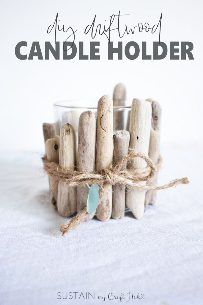 An upcycled driftwood candle holder with small piece of teal sea glass on a white cloth surface.