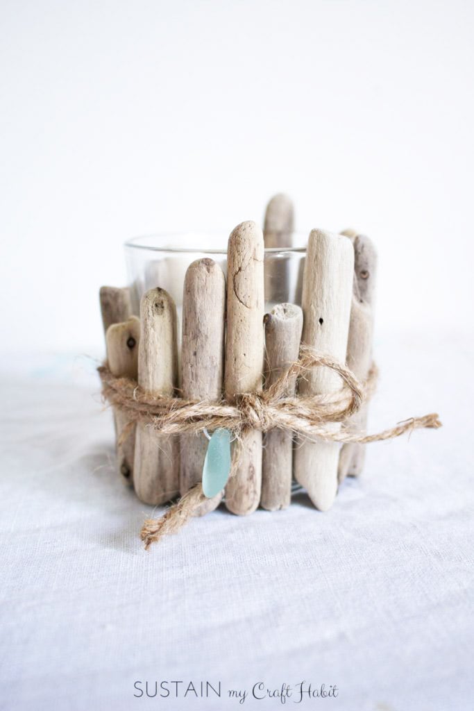 Small driftwood pieces glued onto a glass votive candle as a coastal decorating idea.