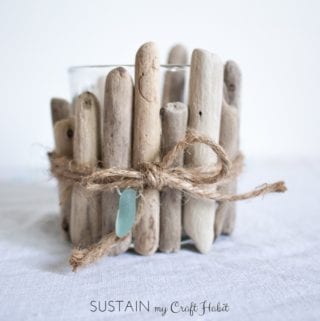 Glass votive candle embellished with rustic driftwood pieces on a white cloth surface