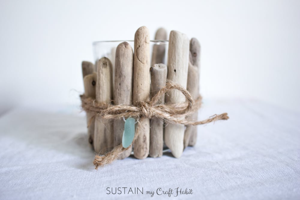 Glass votive candle embellished with rustic driftwood pieces on a white cloth surface