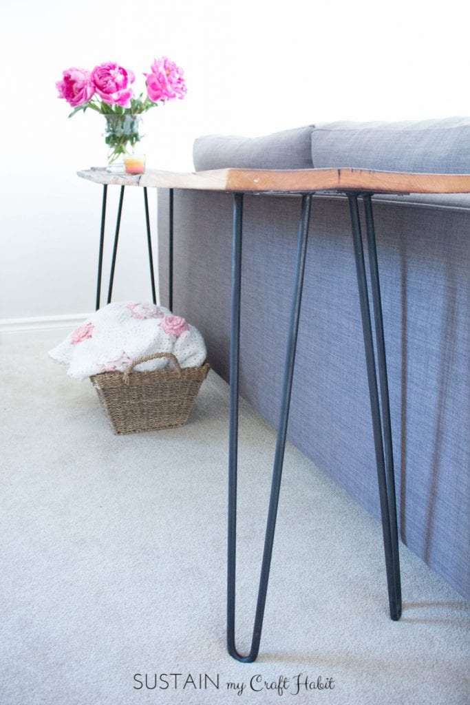 Close up view of a DIY console table placed behind a gray couch with a vase of fresh pink peonies on top