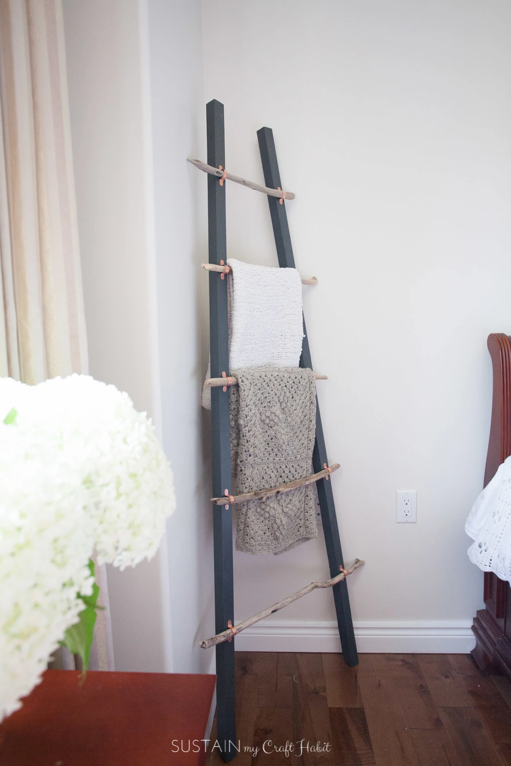 A blanket ladder with gray rails and driftwood rungs leaning against a white wall.