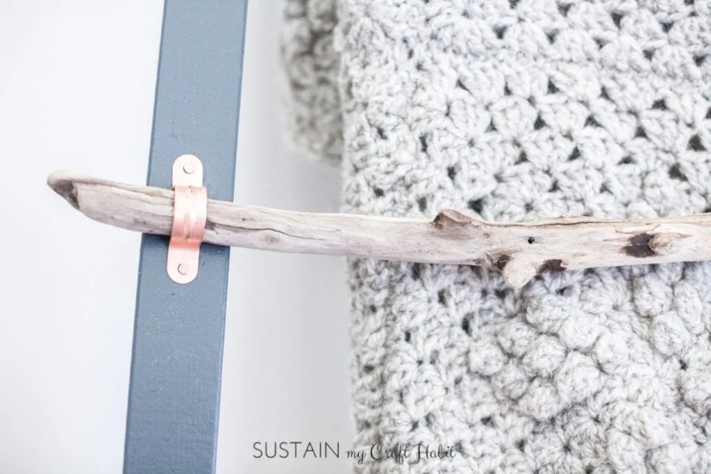 Close up image of a driftwood rung on a DIY blanket ladder.