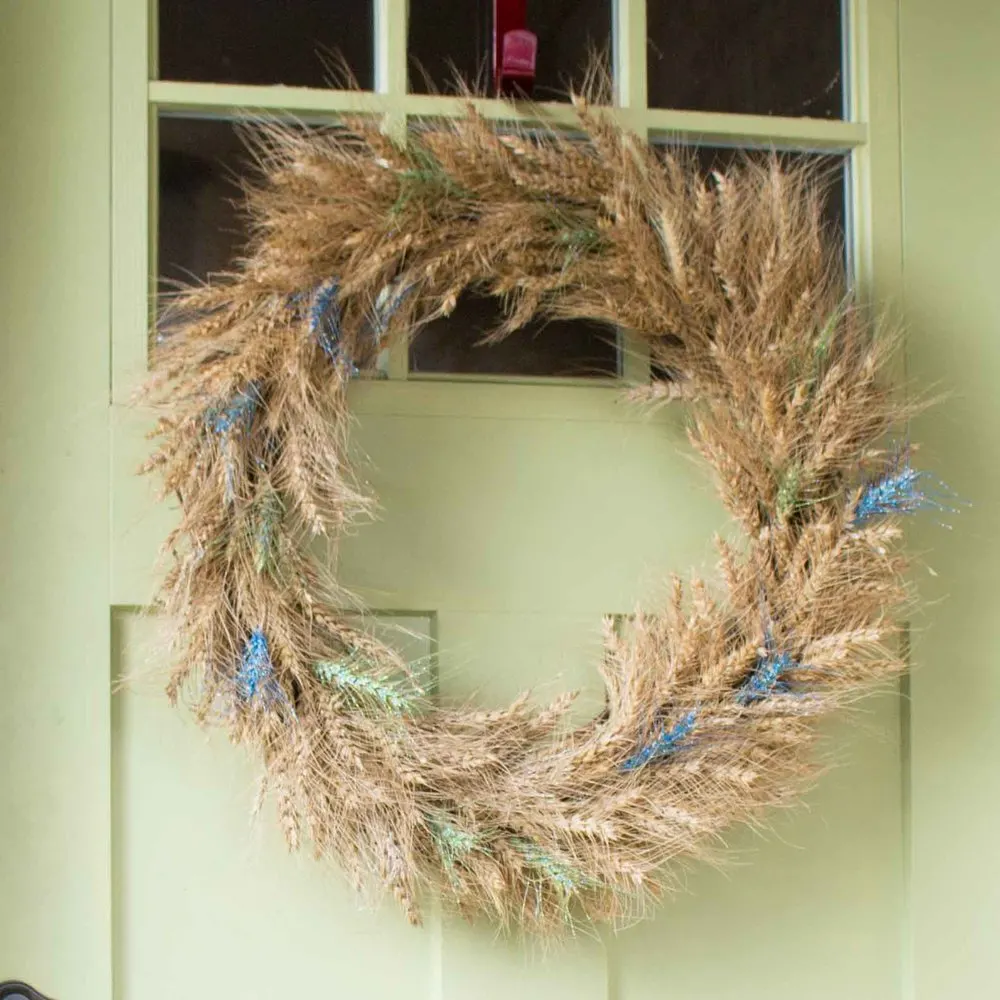 A DIY wheat wreath embellished with paint and glitter hanging on a green front door