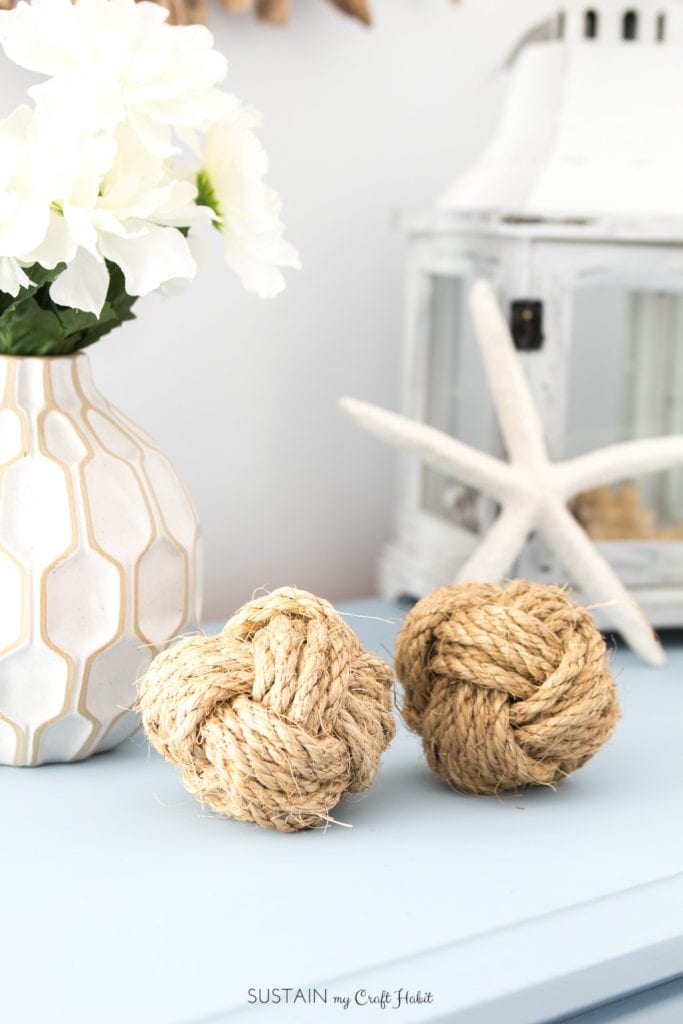 Two DIY monkey's fists nautical rope balls on a blue dresser with coastal home décor in the background