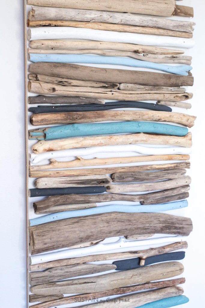 Create a beautiful coastal art piece for your wall using driftwood and a cool mix of blues, white and grey paint.