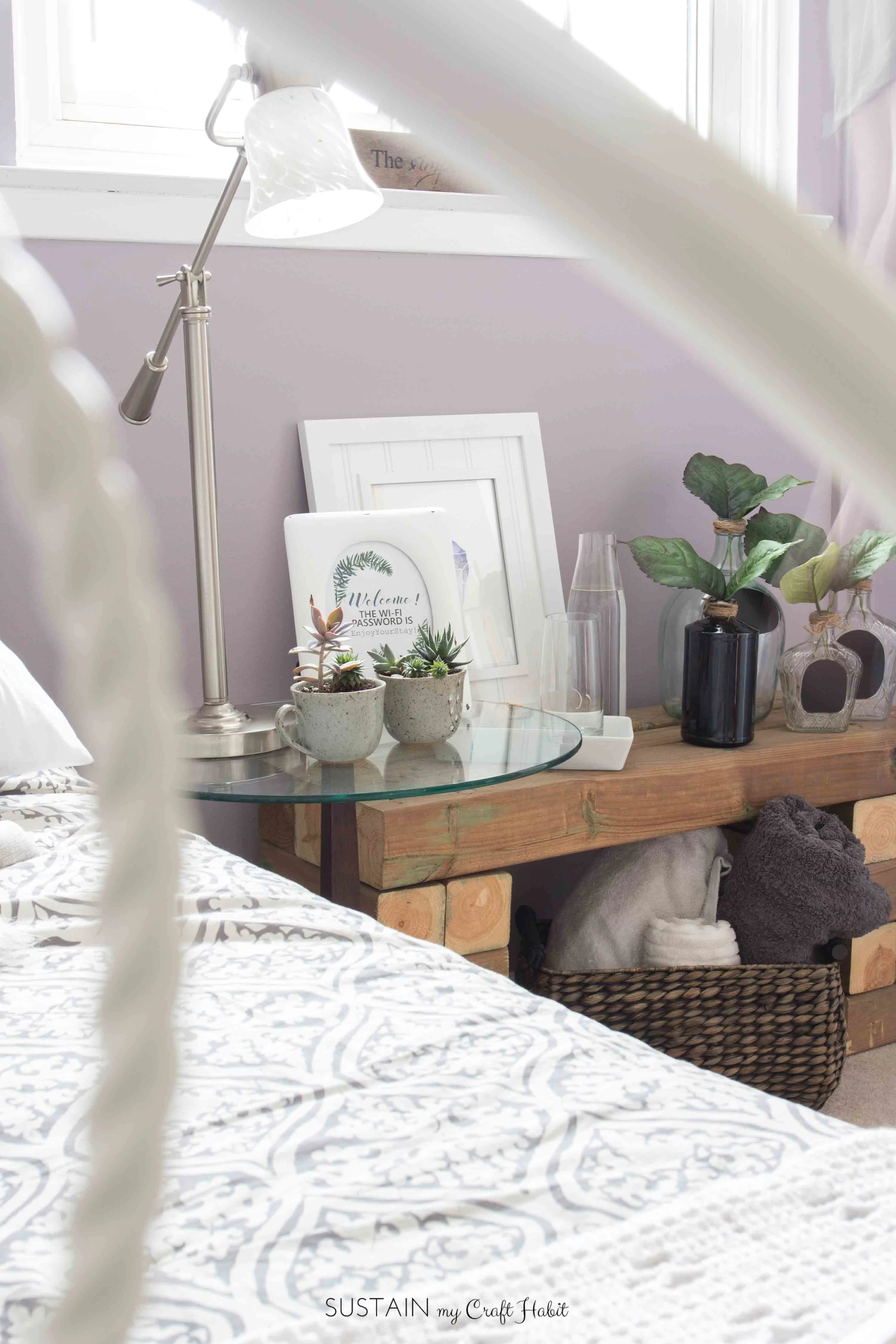 A decorative vignette of photo grames, plants and glass bottles on a wood bench in a guest bedroom.