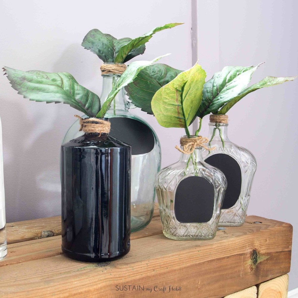 Grouping of clear and black liquor bottle filled with green leaves as a simple bottle decoration idea.