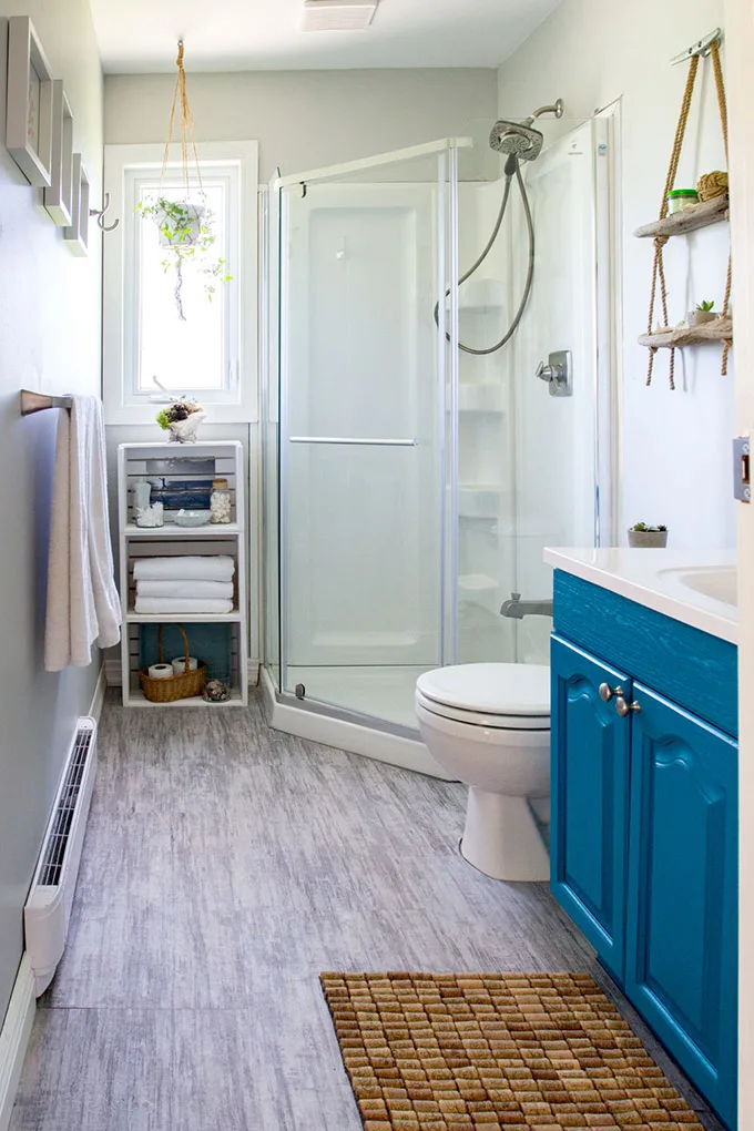 A coastal style bathroom with teal cabinet and grey floors as lake house decorating ideas