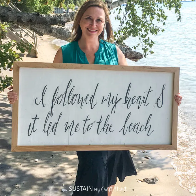 Woman on a beach holding a large handmade wood sign that reads "I followed my heart and it led me to the beach".
