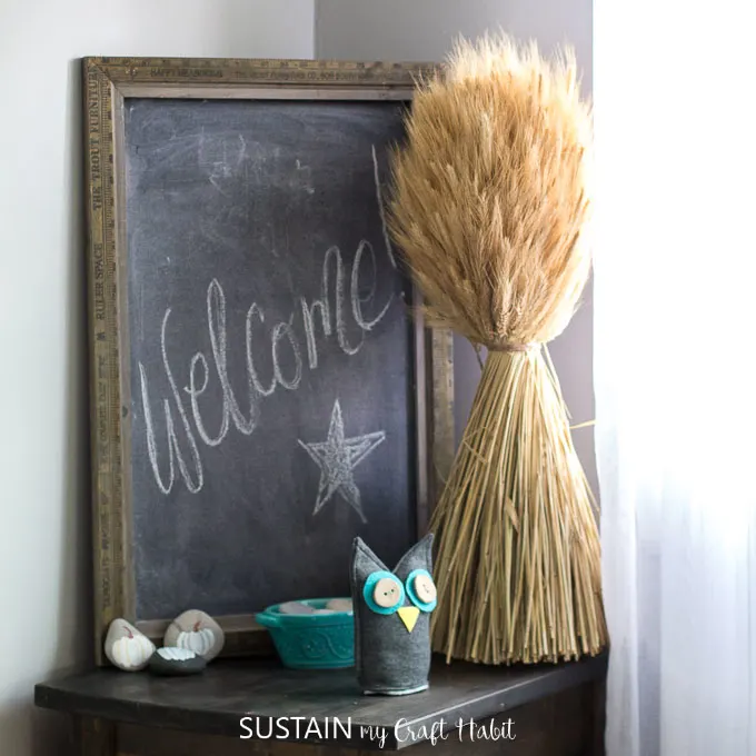 A corner of a room decorated for fall with wheat and a large farmhouse chalkboard
