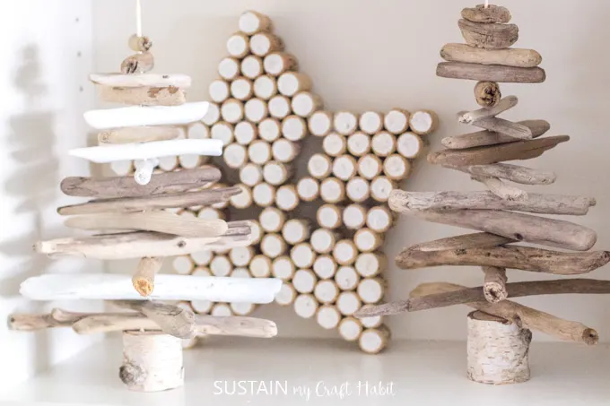 A star made from wine corks behind two small driftwood trees on a white bookshelf