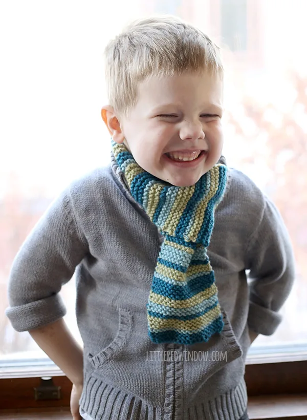 Child smiling and wearing a striped knitted scarf.