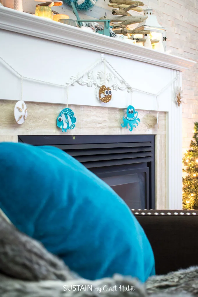 Garland of felt no-sew beach themed ornaments hung on a fireplace mantle with a teal throw pillow in the foreground