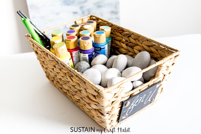 A basket filled with beach stones, paints and brushes as an example of a DIY rock painting kit