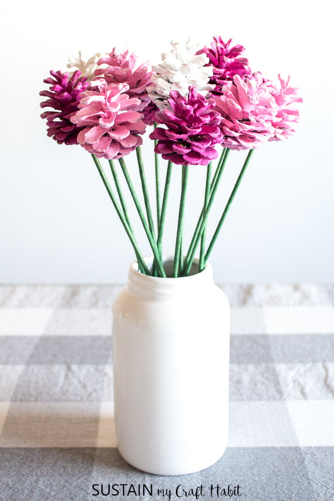 Two-toned pink and white pine cone roses with green stems in a white farmhouse style jar.