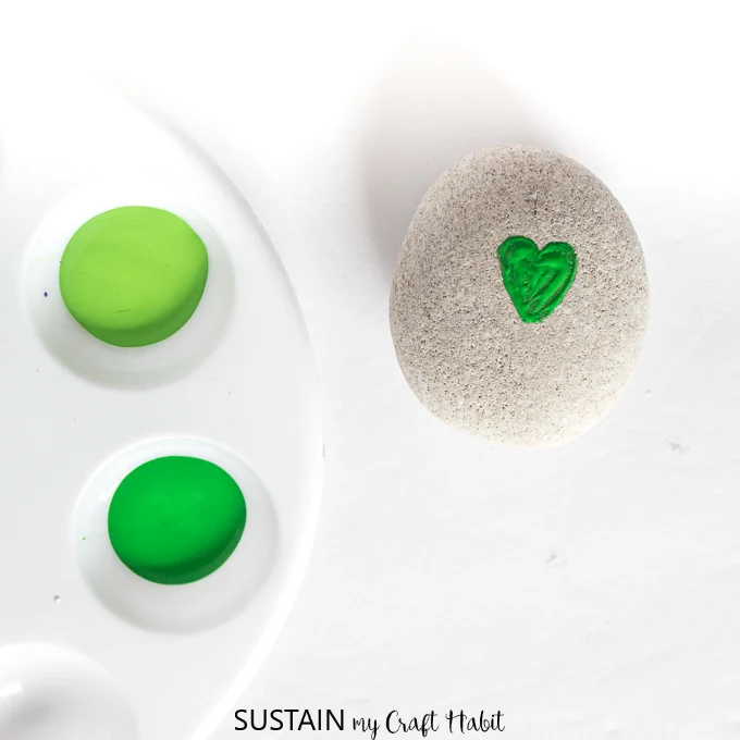 One small green heart painted onto a round gray rock as the start of the shamrock St. Patrick's Day craft idea.