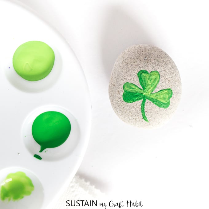 Blending two green paint colors to make the green painted shamrocks on a beach stone.