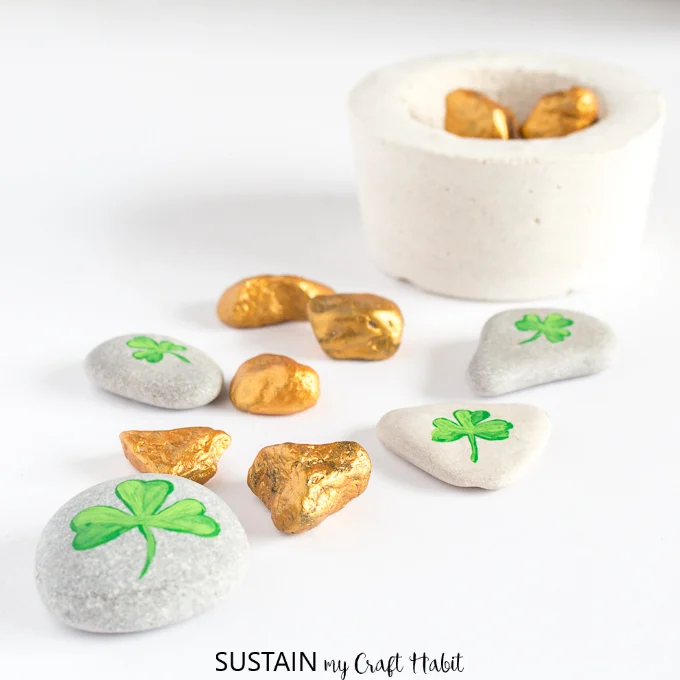 Several gold painted rocks and stones with painted shamrocks on a white surface.