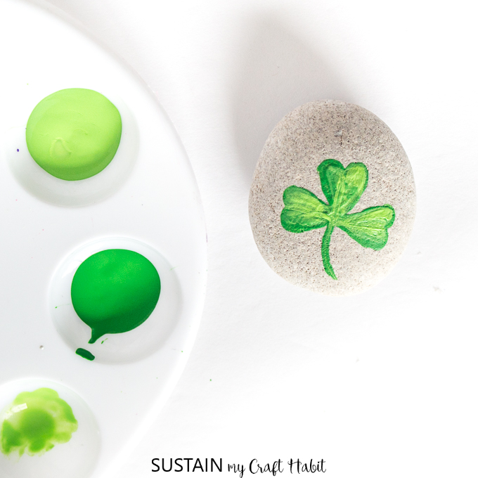 Nearly completed painted shamrock on a small round beach stone.