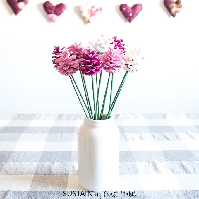 A white jar filled with a bouquet of pink and white pinecone flowers.