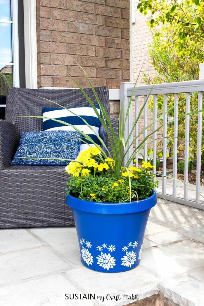A blue flower pot filled with yellow spring flowers on a front porch