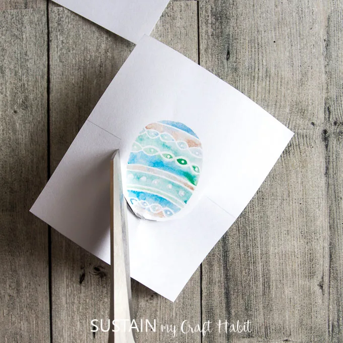 Cutting around a painted Easter egg design with scissors
