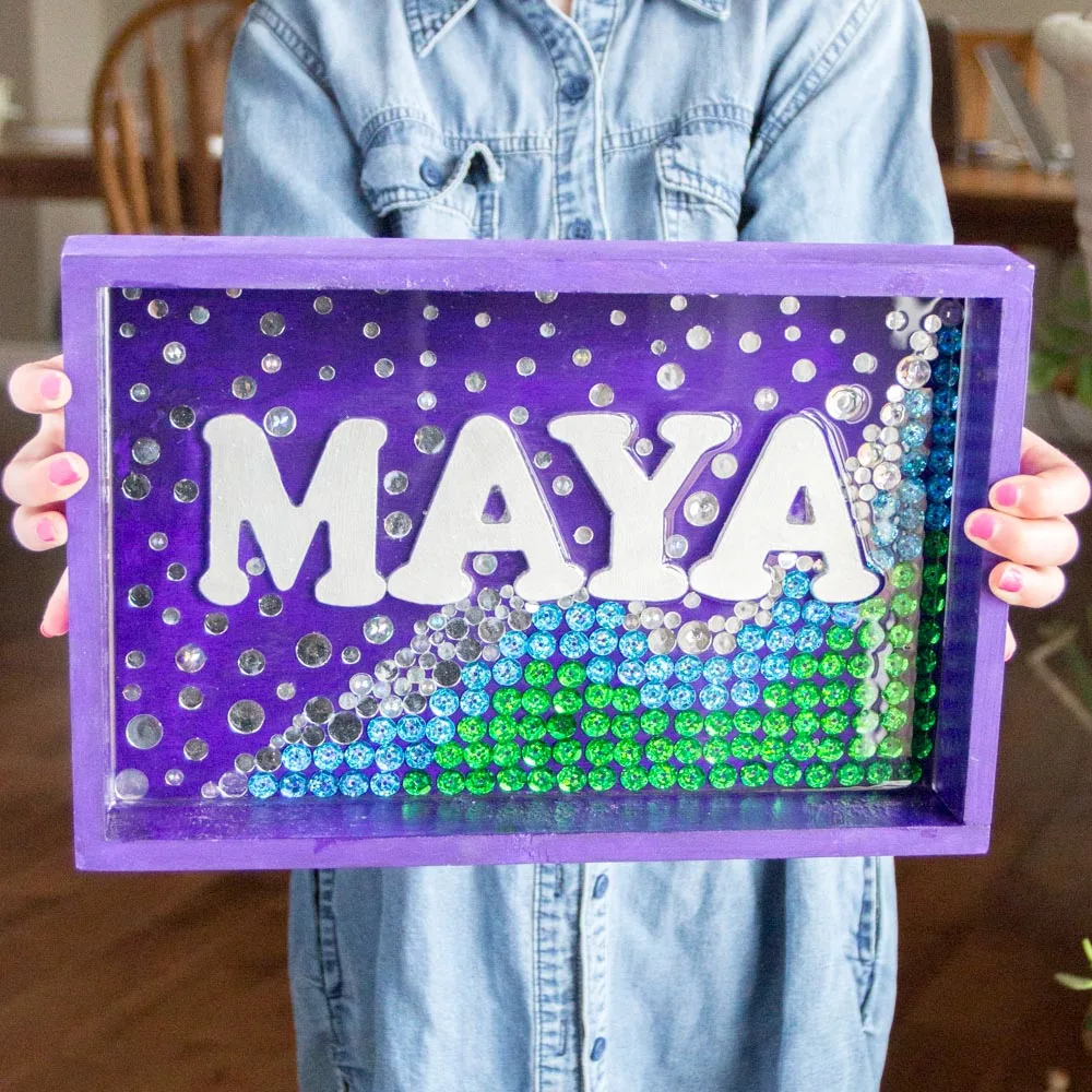 Child holding a personalized mermaid wall art sign in purple, green, blue and silver