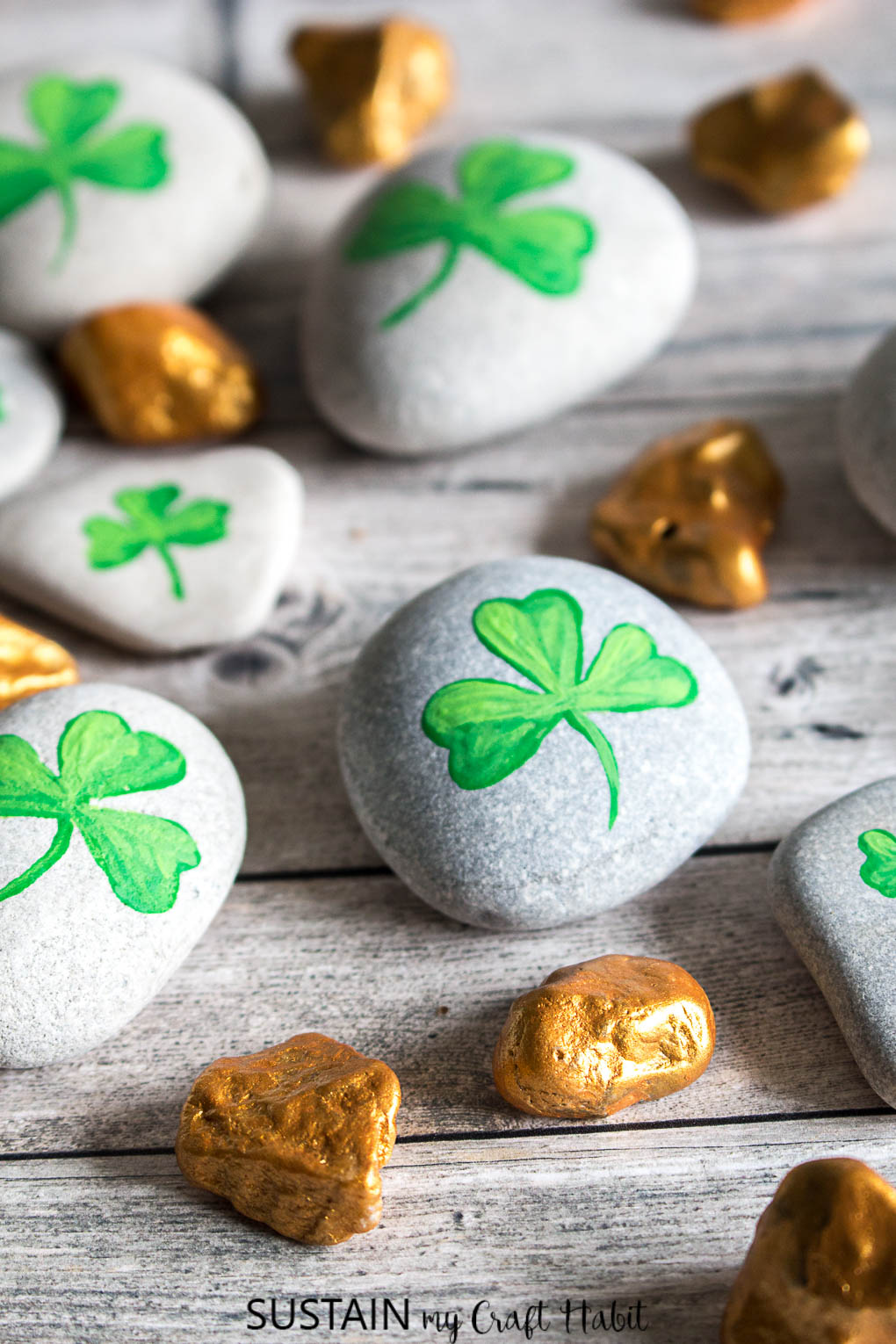 Completed shamrock and gold nugget painted rocks on a grey wood surface as an example of St Patrick's Day crafts ideas.