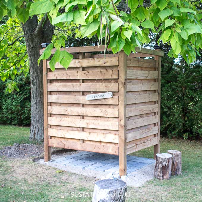 DIY outdoor shower enclosure built of wood slats under a catalpa tree