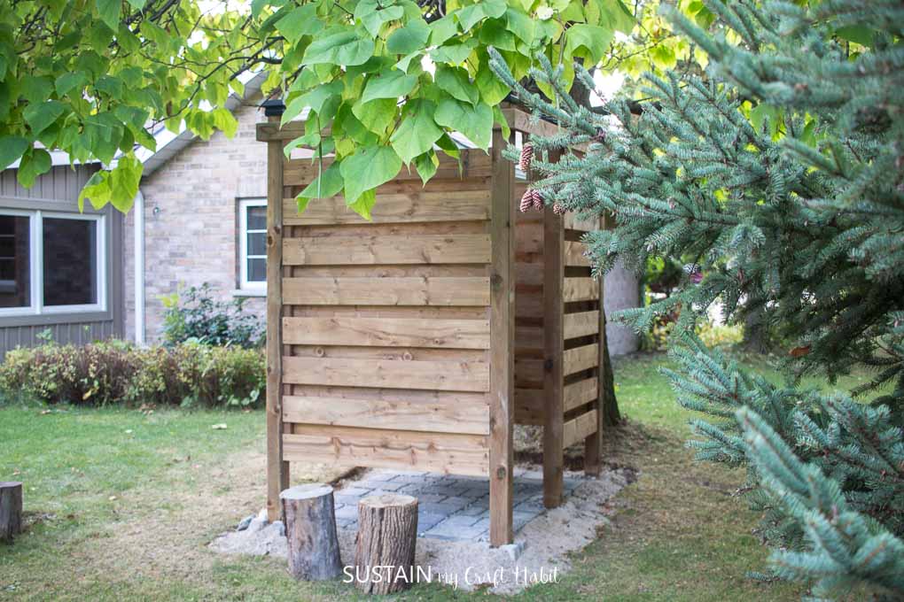 Back view of a wooden outdoor shower enclosure behind a cottage