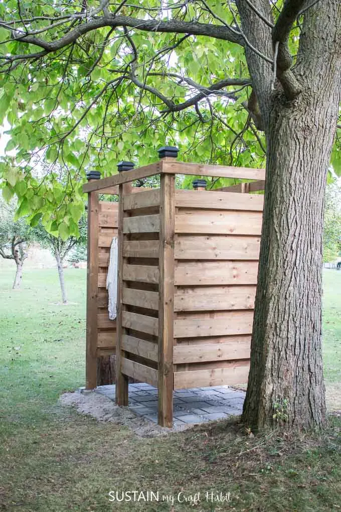 Side profile of a completed wood DIY outdoor shower with a stone base under a tree.