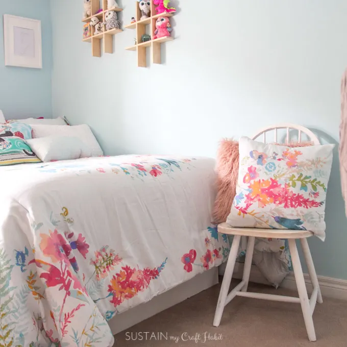 Wooden chair painted which with watercolor-inspired bedding in white, teals and pinks.
