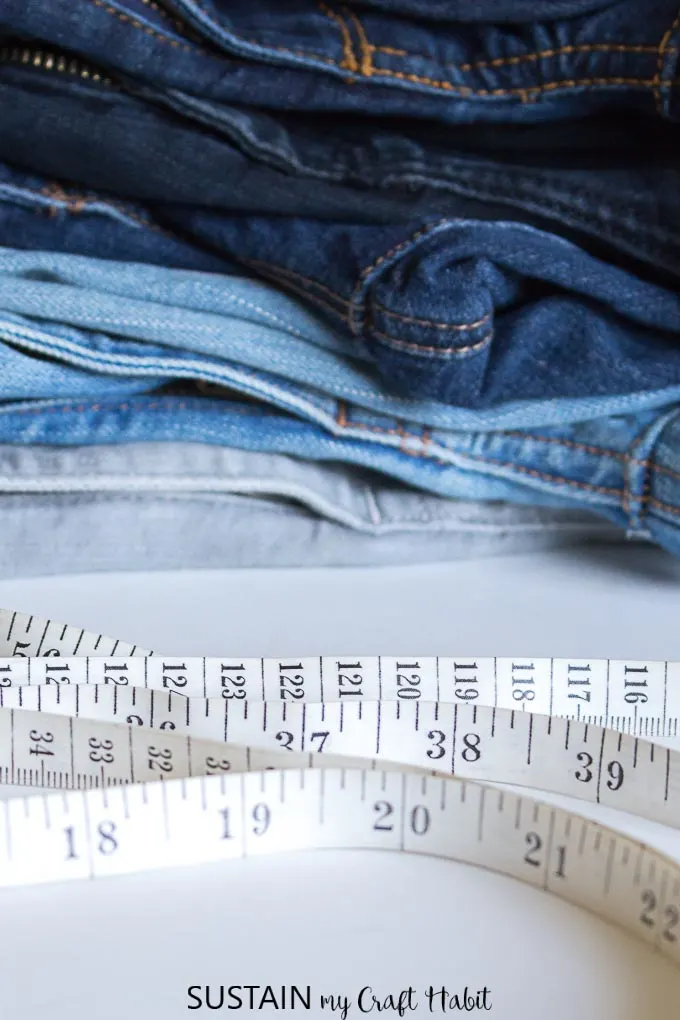 A stack of denim pants in different colors with a measuring tape in front.